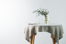 Round Table With A White Tablecloth Decorated With Candles And Decorative Branch. Over A White Wall.