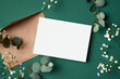 Invitation or greeting card mockup with envelope, eucalyptus and gypsophila flowers on paper background
