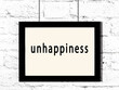 © iushakovsky - Black frame hanging on white brick wall with inscription unhappiness