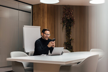 Wall Mural - Tranquil office worker, using his phone during a work break in the conference room.