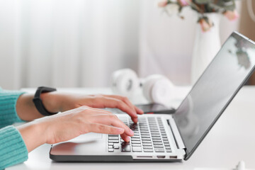 Close up woman hand with green sweater sitting at desk typing on her laptop keyboard. Businesswoman typing on computer at workplace Woman working in home office