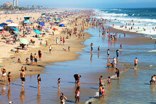 Aerial View Of People Wading In The Ocean Near A Sandy Beach On A Summer Day