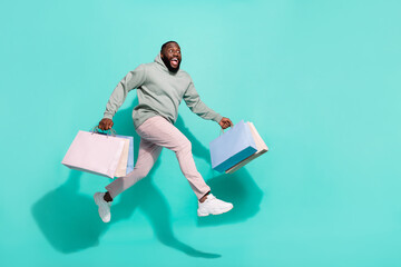 Wall Mural - Full length body size view of attractive cheery trendy guy jumping running carrying bags isolated over vivid teal turquoise color background