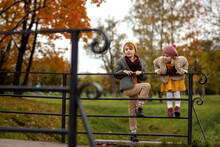 Portrait Of Friendly Romantic Cute Couple Kids Boy And Girl Walking And Playing In Autumn Park. Climb The Fence. Kids Wearing Casual Stylish Clothes. Full Body View.
