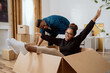 © ABCreative - Happy couple first time home buyers having fun while unpacking boxes of laughter on moving day excited wife driving around sitting in cardboard box while husband pushes her around in new apartment