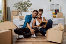 Married Couple After Moving To New House Unpack Boxes Sitting On Floor, Woman Shows Husband Found Photo In Frame From Their Wedding, Man Embraces Wife, They Smile Reminisce