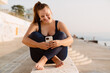 © Drobot Dean - Young ginger woman using mobile phone during yoga practice at seafront