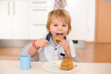 Sticker - Cute preschool boy, blond child, eating piece of cake and drinking milk at home