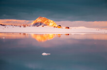 Little Houses Between Fjords In The Snow With Mountain Illuminated By Sunset And Pieces Of Ice Floating In The Sea