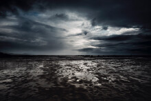 Dramatic Cloudscape And Flood Beach In Dark Night Weather. Stormy And Rainy Sky With Ocean In Background. Epic Seascape With White Sunset Light And Black Clouds.