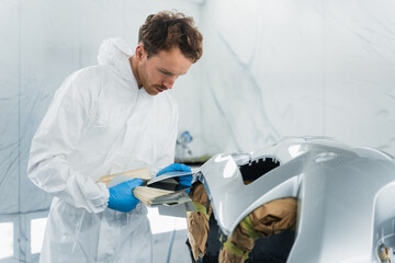 Wall Mural - Auto paint specialist choosing color for car bumper. Man compares the shades of the color of the sample with the color on the bumper of a car