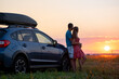 © bilanol - Happy couple standing near their car at sunset. Young man and woman enjoying time together travelling by vehicle