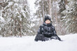 © Lyubov - Happy teenager boy sitting on snow in winter forest. Child having fun outdoors. Joyful adolescent playing in snow at snowfall. Laughing smiling kid walking in winter park in cold weather