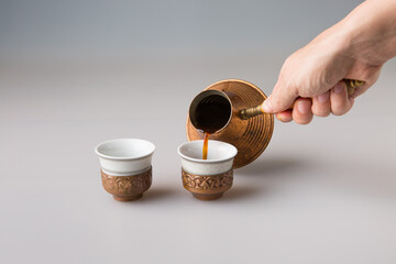 A man's hand pours black cezve coffee into traditional Turkish coffee cups.