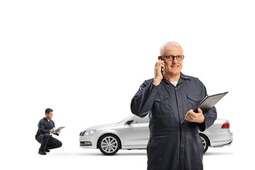 Canvas Print - Car mechanic making a phone call and holding a clipboard and other worker checking a car