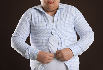 Poster - Overweight man trying to button up tight shirt on dark brown background, closeup