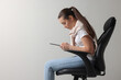 Young woman with poor posture using tablet while sitting on chair against grey background, space for text