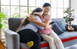 Close up shot of Asian happy lovely young chubby down syndrome autistic autism little daughter smiling hugging cuddling embracing showing warm love with mother sitting on cozy sofa in living room