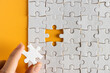 © Hasim Ramle - Hand put last piece of jigsaw puzzle. White unfinished jigsaw puzzle on yellow or orange background.