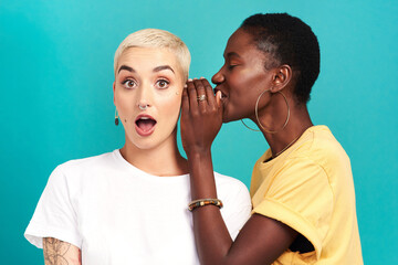 guess what. studio shot of a young woman whispering in her friends ear against a turquoise backgroun