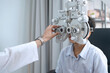 Indian boy looking through optical Phoropter during eye exam, The expert is testing the vision test with diagnostic ophthalmology equipment