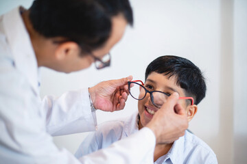 Indian optometrist or optometrist is in white coat helps to get new glasses for boy, child boy in optic store choosing new glasses with optician