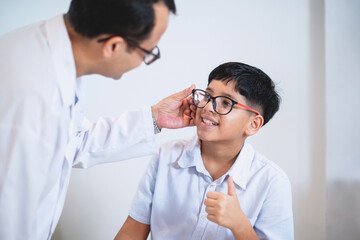 Indian boy try eyeglass frames and thumb up  it's perfect for him, optometrist or optometrist  helps to get new glasses for boy