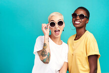 The Future Sure Is Looking Bright. Studio Shot Of Two Young Women Wearing Sunglasses Against A Turquoise Background.