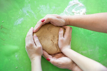 The concept of generational connection, love and care. Close-up over top view of the hands of an elderly woman and a girl who are baking cookies in the kitchen and holding the dough in their hands.