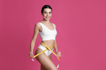 Wall Mural - Young woman measuring waist with tape on pink background. Space for text