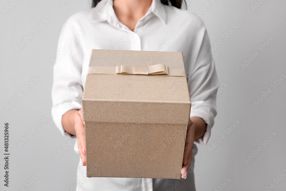 Young woman with gift box on light background, closeup
