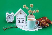 Calendar For February 11: A Decorative House With The Name Of The Month In English, The Number 11, Homemade Cakes, A Cup Of Tea, A Bouquet Of Dried Flowers On An Openwork White Napkin, An Alarm Clock