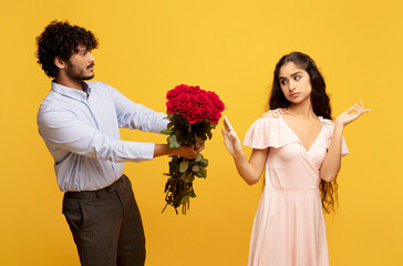 Wall Mural - Unwanted confession. Displeased indian lady rejecting her admirer with roses on Valentine's Day, yellow background