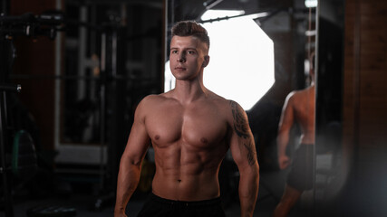  Handsome young athlete man bodybuilder with naked muscular torso trains in the gym on a dark background