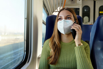 Canvas Print - Young business woman wearing protective mask required for public transport talking with phone sitting in the train