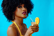 © Carlos David - beautiful young African American woman in bright summer outfit drinking refreshing cocktail isolated on blue background