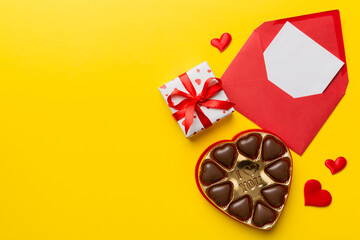 Envelope on colored background for Valentine Day with gift box and chocolate. Heart shaped with gift box of chocolates top view with copy space