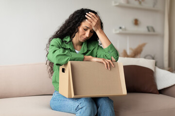 Wall Mural - Frustrated Woman Buyer Unpacking Cardboard Box Siting On Couch Indoor