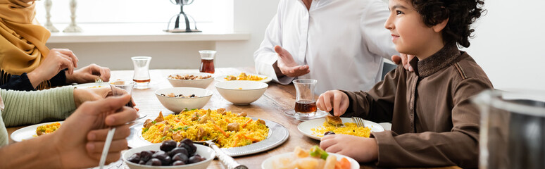 Wall Mural - arabian boy smiling during dinner with muslim family at home, banner.