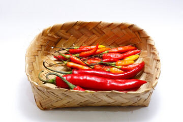 Wall Mural - Big red chilies and cayenne pepper are placed in a traditional container made of woven bamboo. Isolated on white background