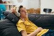 © cherryandbees - teenager boy listening music on headphones and relaxing on sofa at home