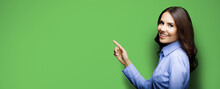 Portrait Of Smiling Young Businesswoman. Brunette Girl Pointing Showing By Index Finger Copy Space Area For Text, Isolated On Green Color Background. Wide Banner Composition Image.