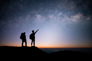 Wall Mural - Silhouette of young couple traveler and backpacker standing and watched the star and milky way on top of the mountain. He enjoyed traveling and was successful when he reached the summit.