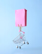 A pink shopping bag carries a shopping trolley on a blue background. Sales aesthetic shopping cart concept