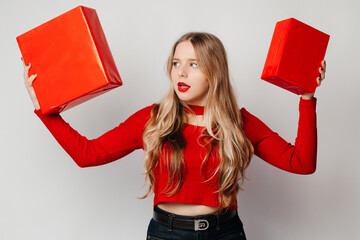 Thoughtful elegant young woman standing with two with gift boxes, looking at the present, with open mouth. Choosing a gift for the holiday for her boyfriend. Valentines Day present concept