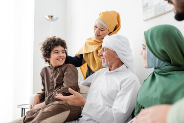 Wall Mural - mature muslim man in turban talking to arabian grandson near happy interracial family.