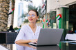 Young beautiful woman in eyeglasses working on laptop and sitting in cafe outdoors People and technology. Lifestyle concept
