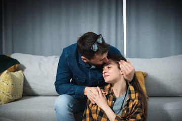 Young couple in love a woman sitting on the floor and a guy on the couch kisses her gently massages her shoulders and head to relax her muscles after a hard day at work and to relieve her of stress.