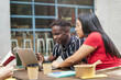 © EFStock - Young coworkers digital entrepreneurs working together during meal break. African and latin students using laptop for project