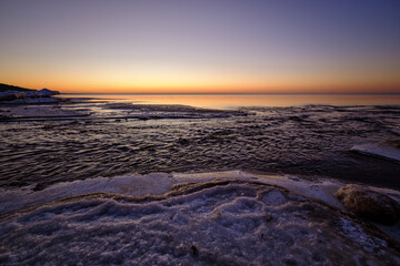 Wall Mural - colorful beautiful sunset at sea in winter with snow on the beach